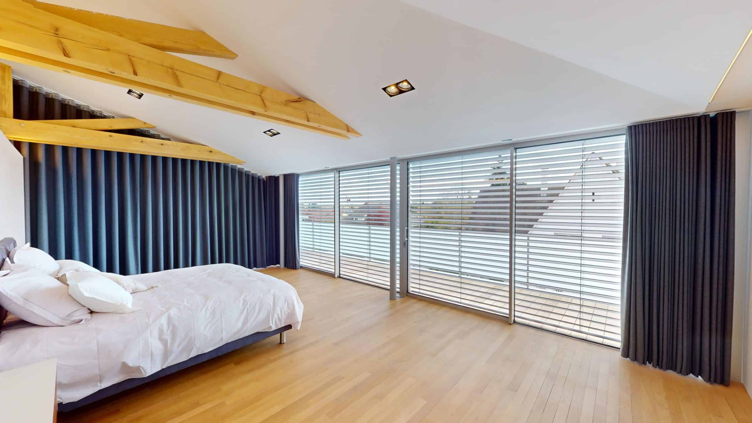 Chambre spacieuse avec grand lit et fenêtres offrant une vue panoramique sur Colmar.