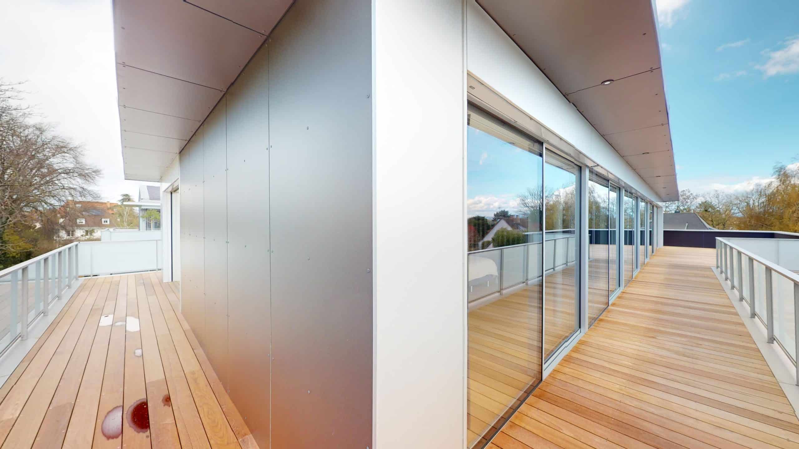 Balcon en bois avec grandes fenêtres et vue sur la nature environnante.